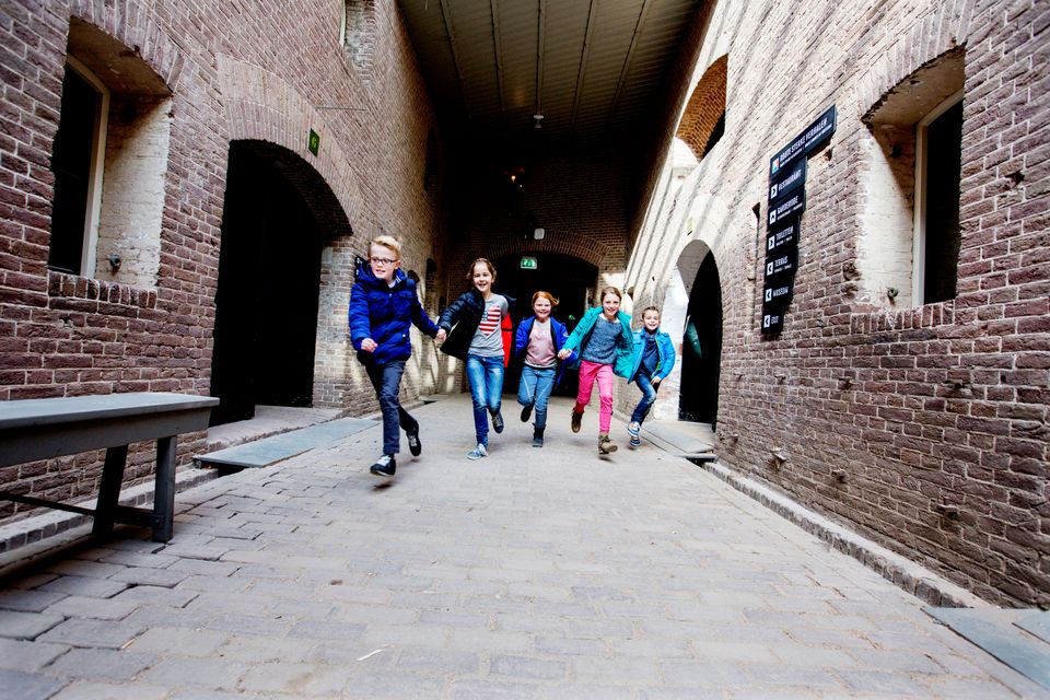 Een groep kinderen rent door een gang van baksteen in een fort.