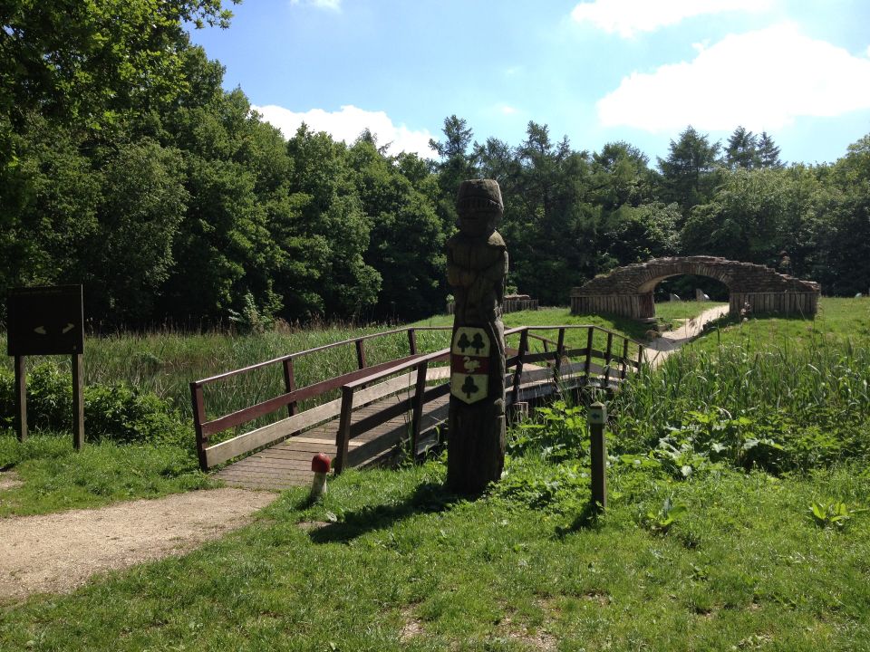 Een groen landschap waar een bruggetje leidt naar een oude ruïne wat lijkt op een viaduct in Bant in de Noordoostpolder.