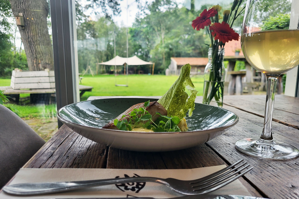 Een gedekte tafel met een glas witte wijn en een mooi opgemaakt bord met eten.