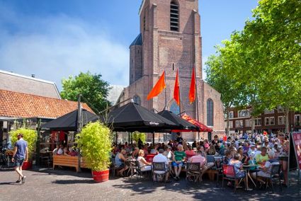 Volle terrassen op het Kerkplein in Woerden met uitzicht op de Grote Kerk tijdens een zonnige dag.