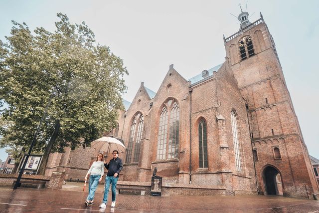 Een man en een vrouw lopen met een paraplu in de regen, op de achtergrond een grote kerk.
