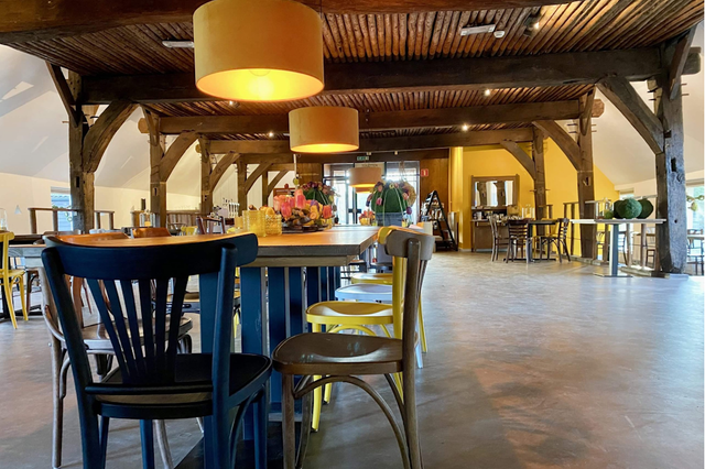 In de eetzaal van een restaurant met oude gebinten staat een lange tafel met verschillende houten stoelen.