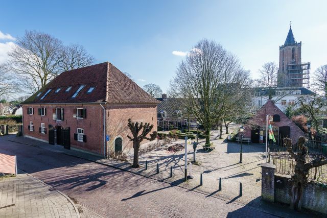 Uitzicht op de historische Napoleonschuur en het plein in het centrum van Amerongen, met de toren van de Andrieskerk op de achtergrond. De karakteristieke bebouwing en klinkerstraten geven een goed beeld van de historische dorpskern.