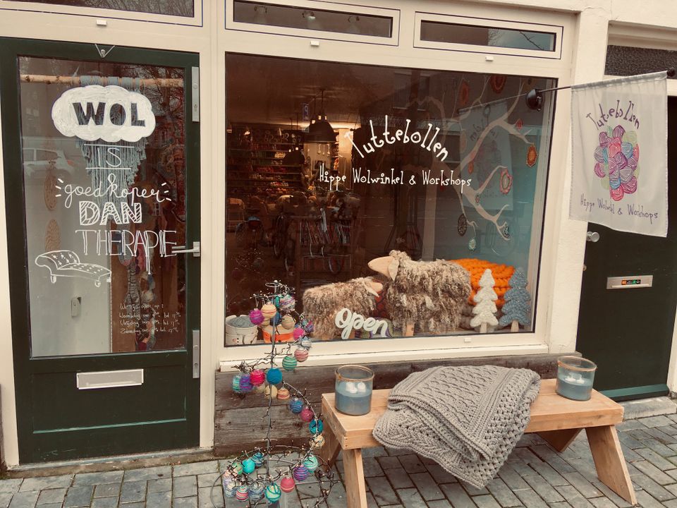 Winkel Tuttebollen in Woerden, Groene Hart, etalage van een hippe wolwinkel met bollen wol, handgemaakte decoraties en informatie over workshops breien en haken in het centrum.