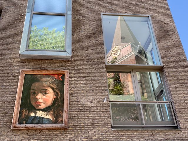 Schilderij van Emmetje, de zus van Leo van Gestel, aan een gevel in Woerden met in het raam de reflectie van de Petruskerk.