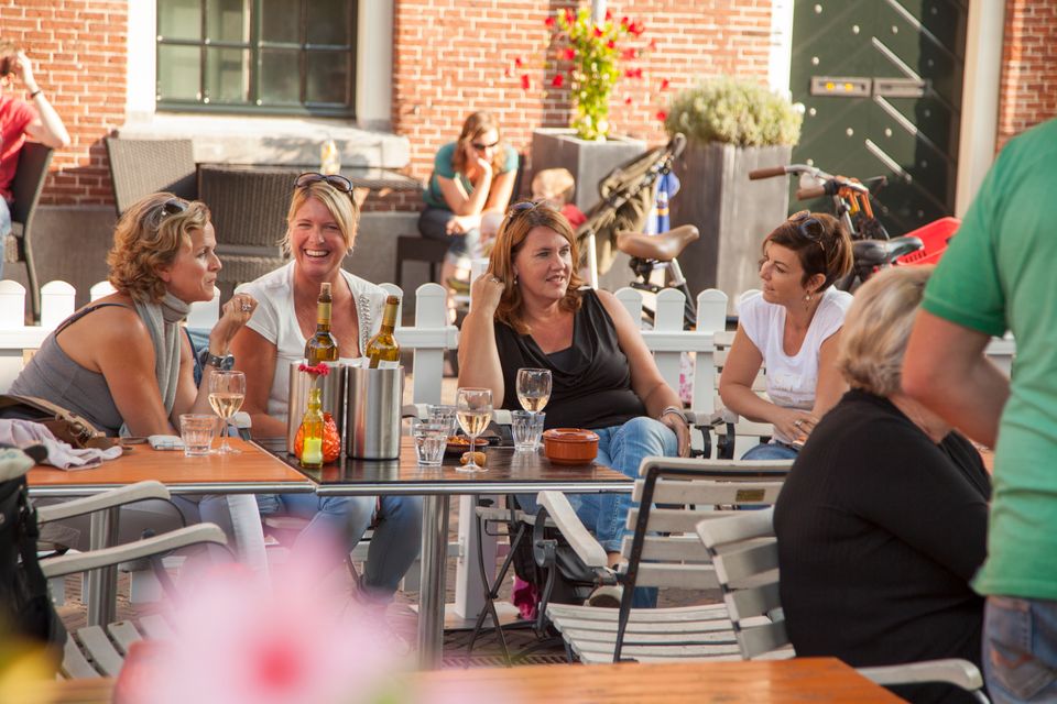 Vrouwen op een terras met een glas rosé, lachend en kletsend met elkaar, omringd door andere mensen op een terras op een zomerse dag.