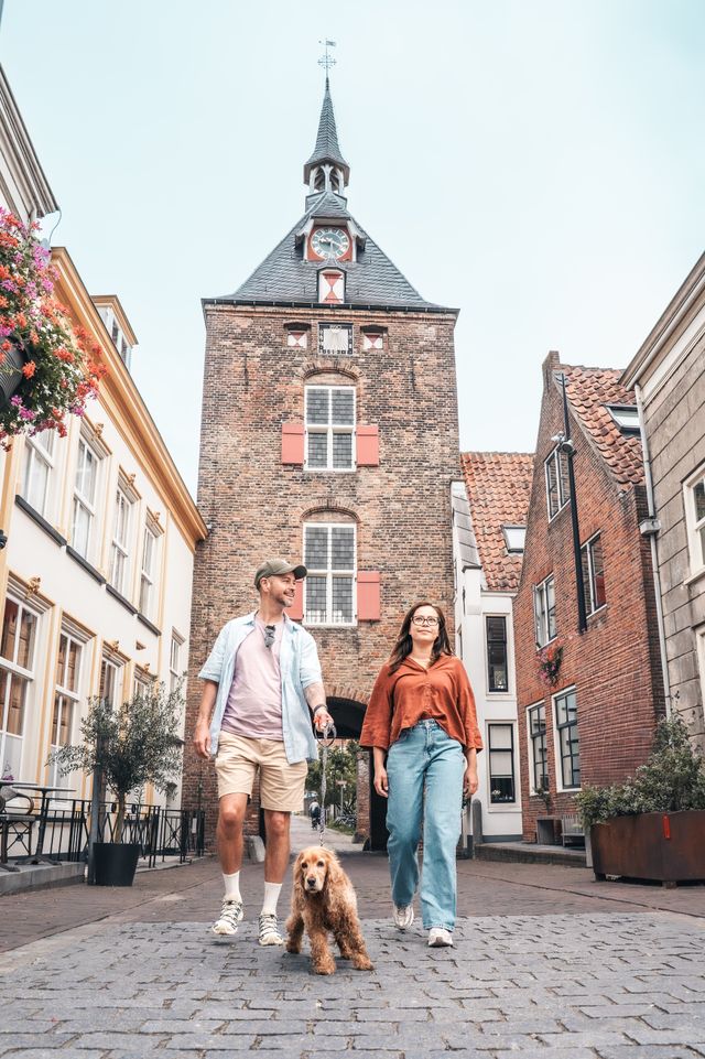 Een man en een vrouw lopen met een hond onder een historisch gebouw door.