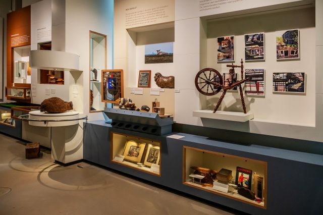 Tentoonstellingsruimte in Stadsmuseum Veenendaal met objecten, foto’s en een spinnewiel over de lokale wol- en textielgeschiedenis. De museumopstelling laat zien hoe deze industrie belangrijk was voor de ontwikkeling van Veenendaal.