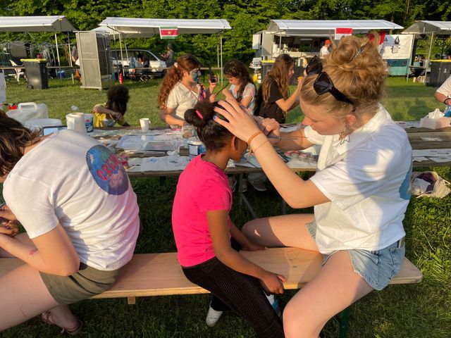 Een jonge meid schminkt een klein meisje tijdens Wereld BBQ dag