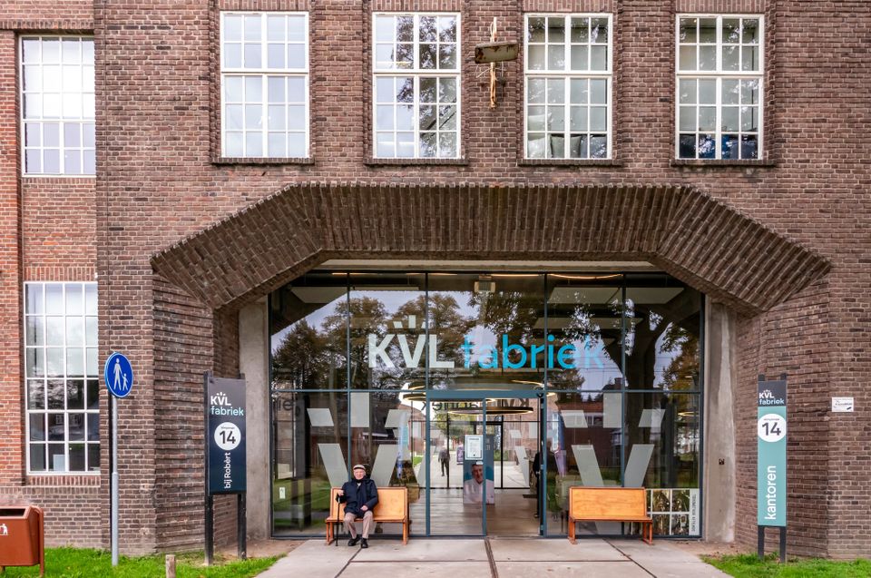 Voorkant monumentale hoofdgebouw KVL fabriek in Oisterwijk met man op bankje ervoor