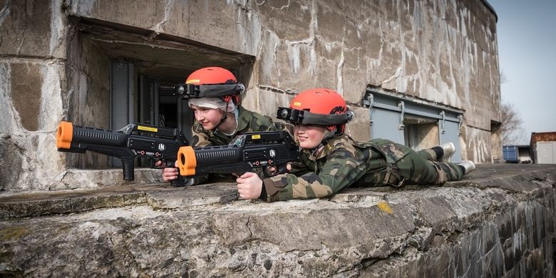 Twee jongetjes in legeroutfits liggen op een betonnen fort met grote laser guns.
