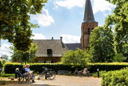 Fietsers pauzeren op een bankje in Helvoirt vlakbij de kerk