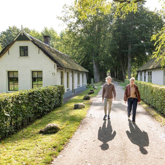 Man en vrouw wandelen op het voetpad tussen de ambtenarenhuisjes in Frederiksoord