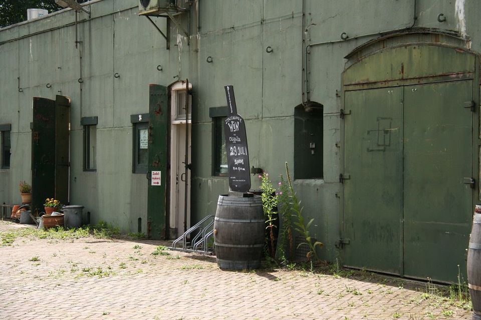 Een betonnen fort met groene luiken en twee krijtbordjes voor de deur.