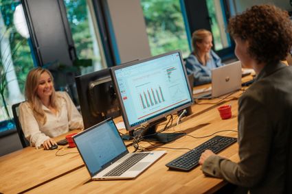 Collega's zitten aan het bureau te werken en op het scherm van de computer zie je een grafiek.