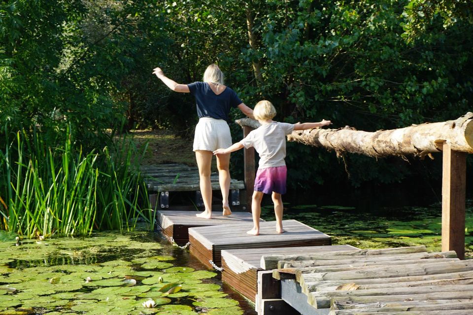 Moeder en kind balanceren samen op het blotevoetenpad bij Buitenplaats Kameryck, omgeven door groene natuur en waterlelies.