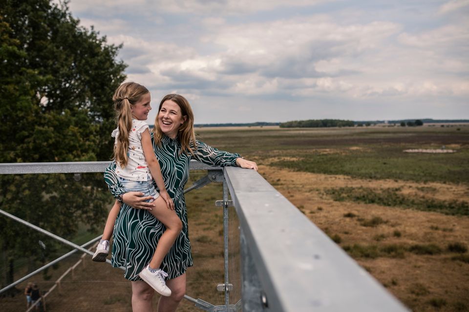 Moeder staat met dochter op de arm bovenop een uitkijktoren naar de natuur te kijken.