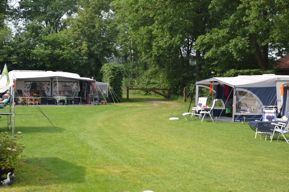 Groot groen grasveld met aan de zijkanten 2 caravans met voortenten en zitjes.