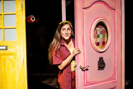 Theatervoorstelling Het Muizenhuis: Sam & Julia op avontuur in Het Klooster in Woerden, Groene Hart, kleurrijk decor met een actrice die nieuwsgierig door een roze deur kijkt tijdens een familievoorstelling voor kinderen.