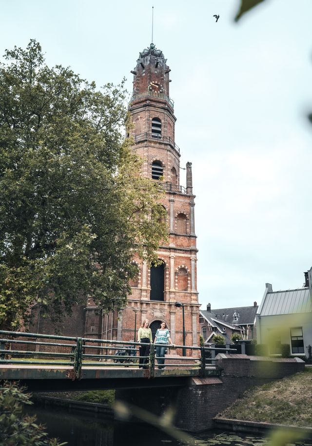 Historische Oude Nicolaaskerk in IJsselstein, Groene Hart. Monumentale bakstenen kerktoren met brug over de gracht, twee wandelaars en sfeervol stadsgezicht in de historische binnenstad.
