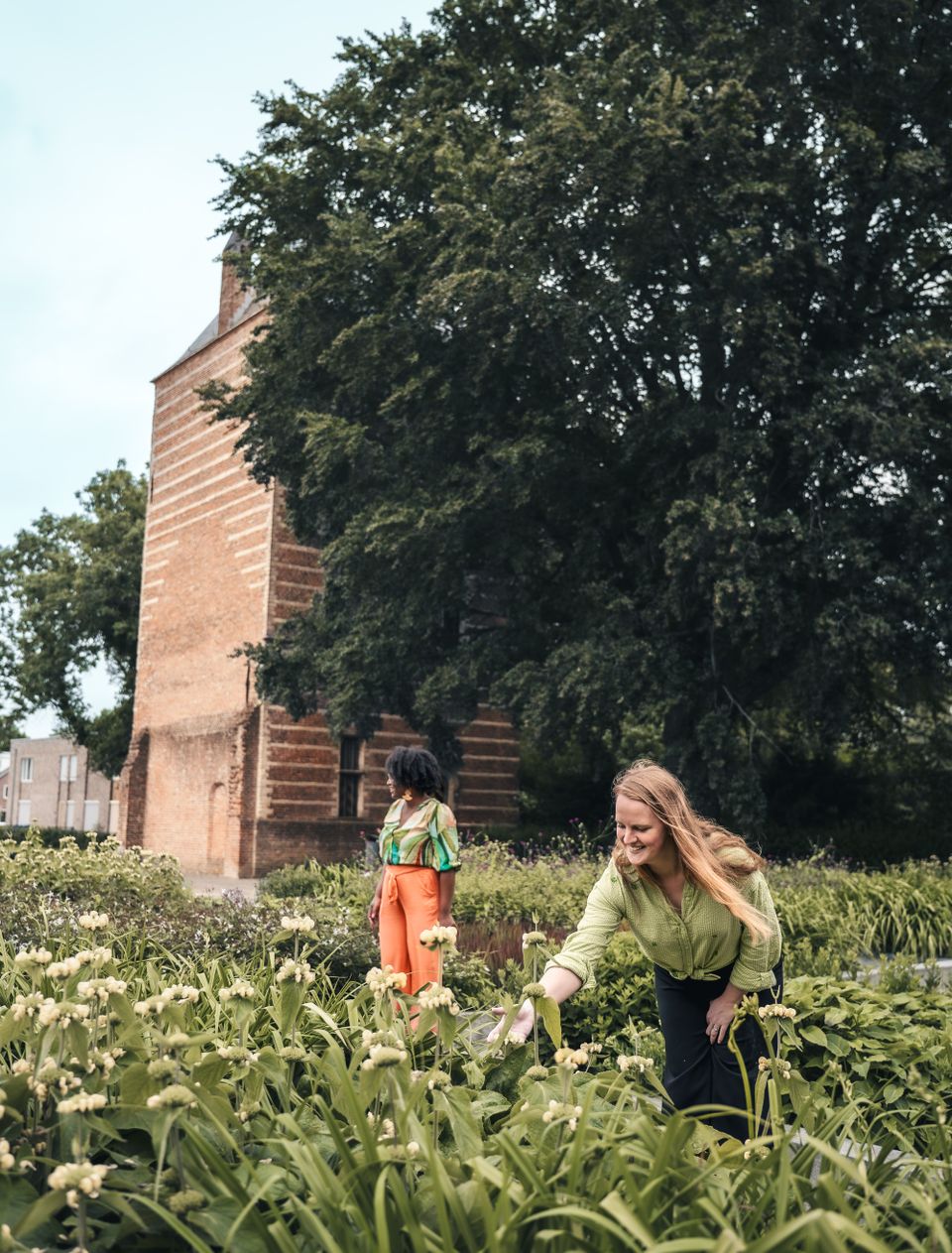 Twee vrouwen staan voor Kasteeltoren IJsselstein en bekijken de bloeiende bloemen in de tuinen om de toren heen
