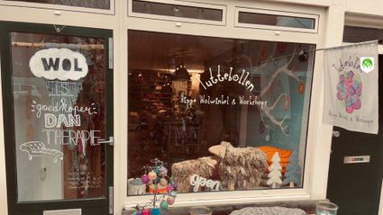 Winkel Tuttebollen in Woerden, Groene Hart, etalage van een hippe wolwinkel met bollen wol, handgemaakte decoraties en informatie over workshops breien en haken in het centrum.