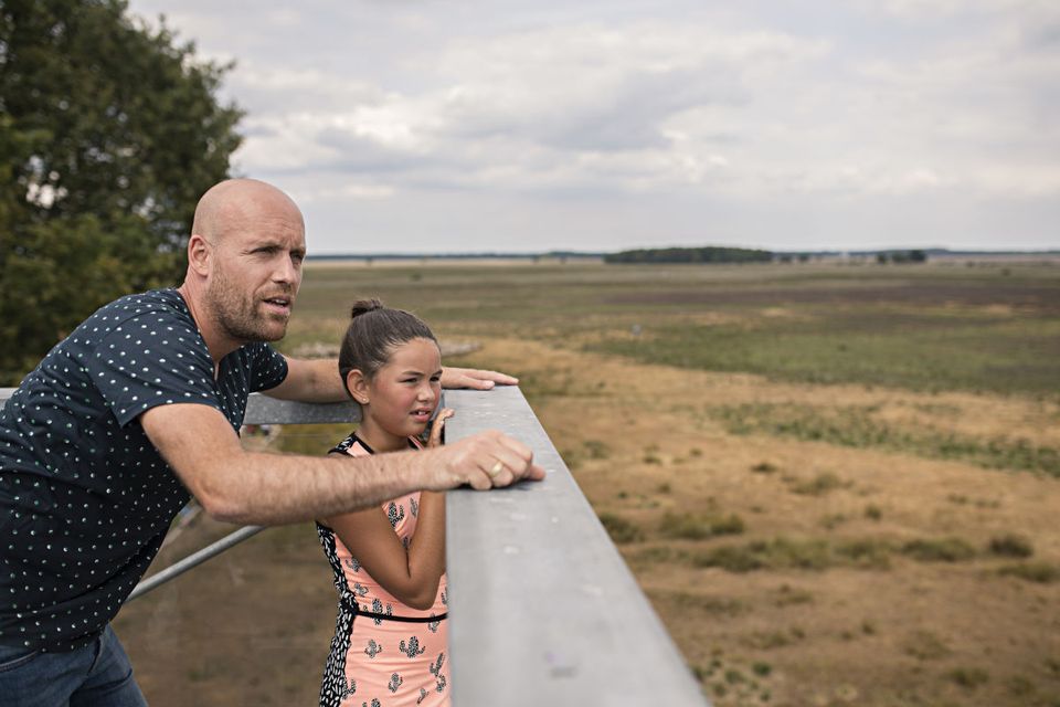 Man en kind kijken uit over het uitzicht vanaf de uitkijktoren op het Dwingelderveld.