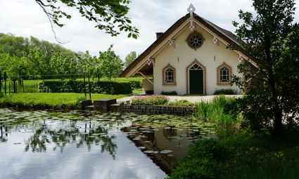 Een rietgedekt historisch huisje aan het water van Natuurhuisje Elsehof Logies, omringd door groen en waterplanten in het landelijke Groene Hart.