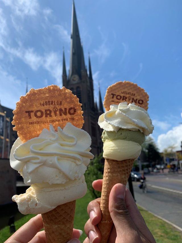 Twee hoorntjes met ambachtelijk ijs van IJssalon Torino, met op de achtergrond de Bonaventurakerk in Woerden op een zonnige dag.
