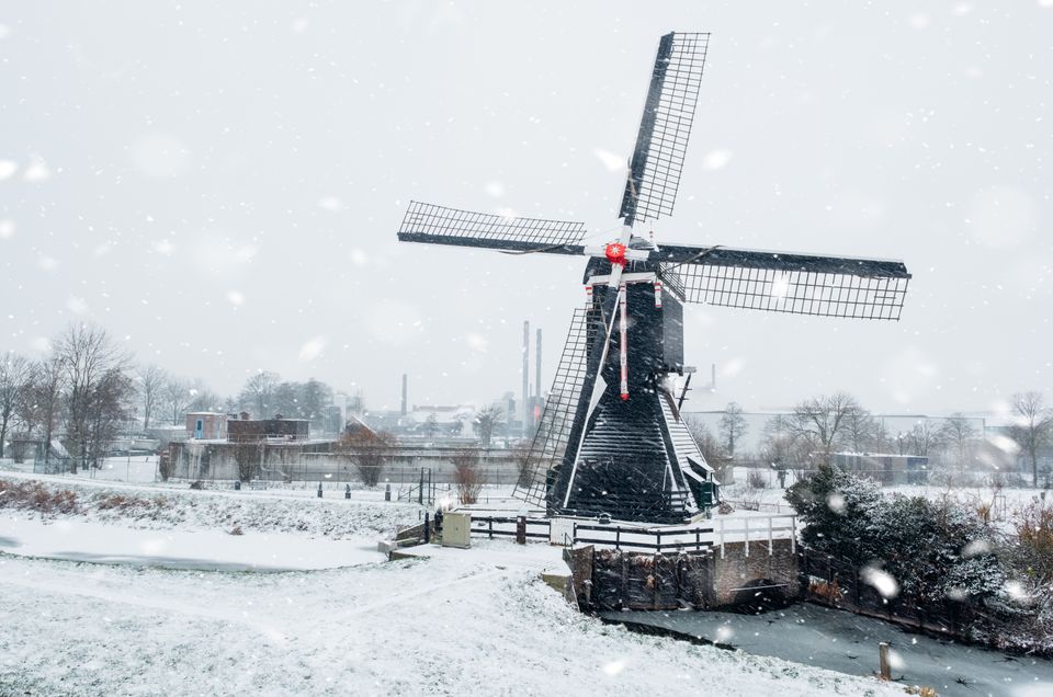 Molen in Leerdam tijdens een sneeuwbui. De wieken steken af tegen de witte lucht, en het landschap is bedekt met een laag sneeuw – winter in het Groene Hart.