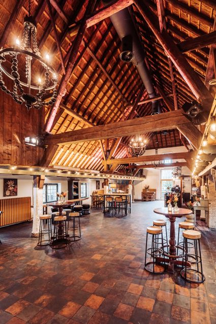 Zakelijke locatie De Willemshoeve in Woerden, Groene Hart, ruime historische zaal met hoge houten kapconstructie, kroonluchters, statafels en sfeervolle verlichting.