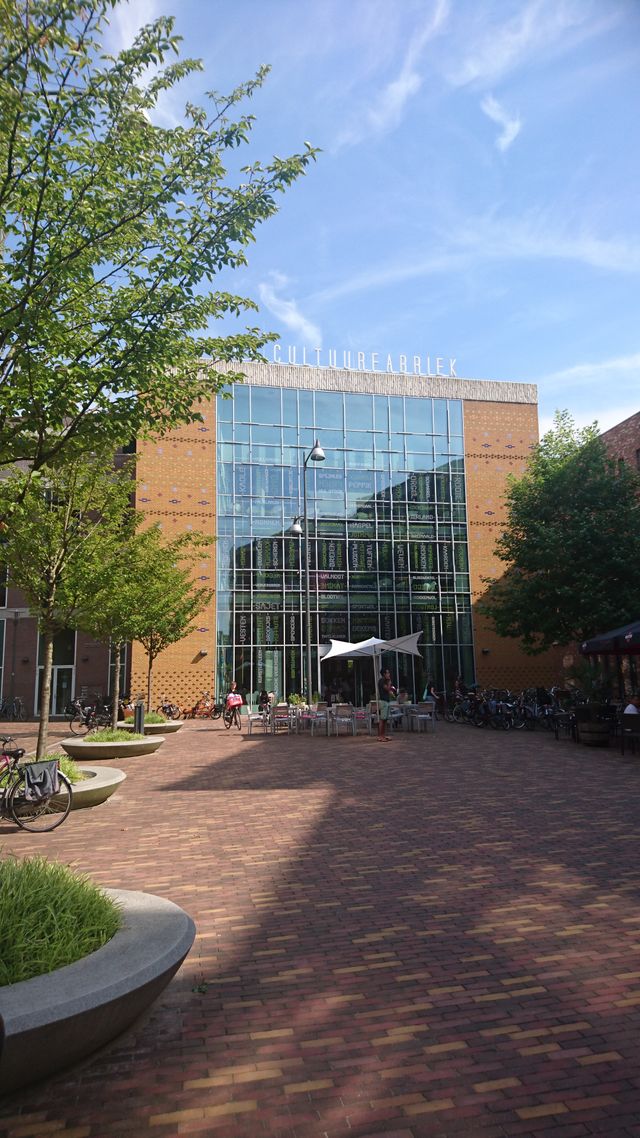 De Cultuurfabriek in Veenendaal aan een sfeervol plein met groen, terrassen en fietsen. De foto laat een culturele ontmoetingsplek in het centrum van Veenendaal zien.