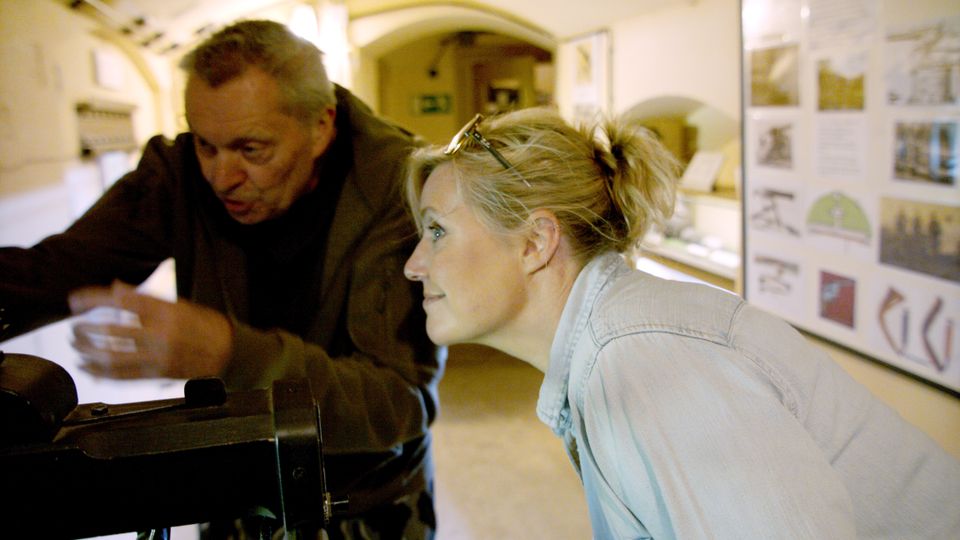 Een man en een vrouw staan samen gebogen over een model van een mitrailleur in een fort.