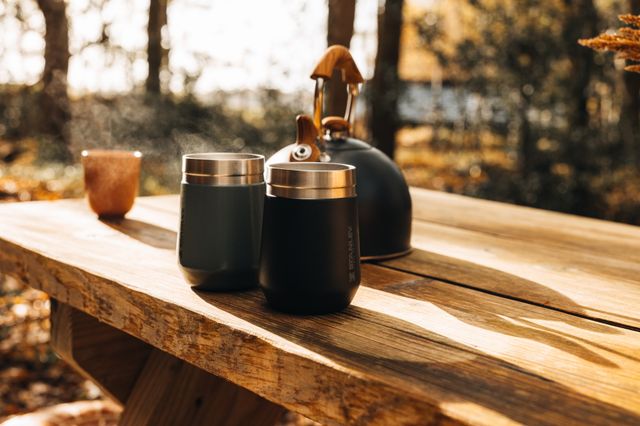 Een theepot met kopjes op een houten tafel op een terras van een accommodatie in het bos.