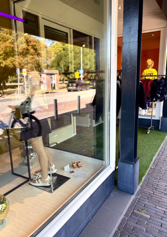 Etalage van een modewinkel in Woerden met mannequin in sportieve outfit, witte sneakers en discoballen als decoratie.
