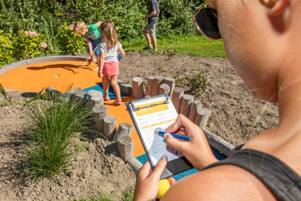 Twee kinderen die minigolf spelen en de derde die de score noteert, bij BatensteinBuiten in een groene omgeving op een zomerse dag.