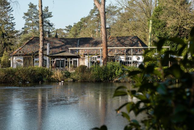 Vooraanzicht van de horeca Hermitage Oisterwijk met terras en een vijver en groen