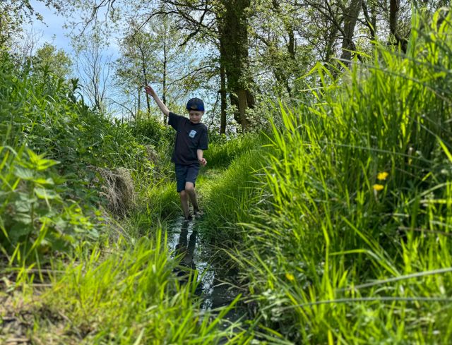 Jongetje loopt door een smal slootje met groen gras.