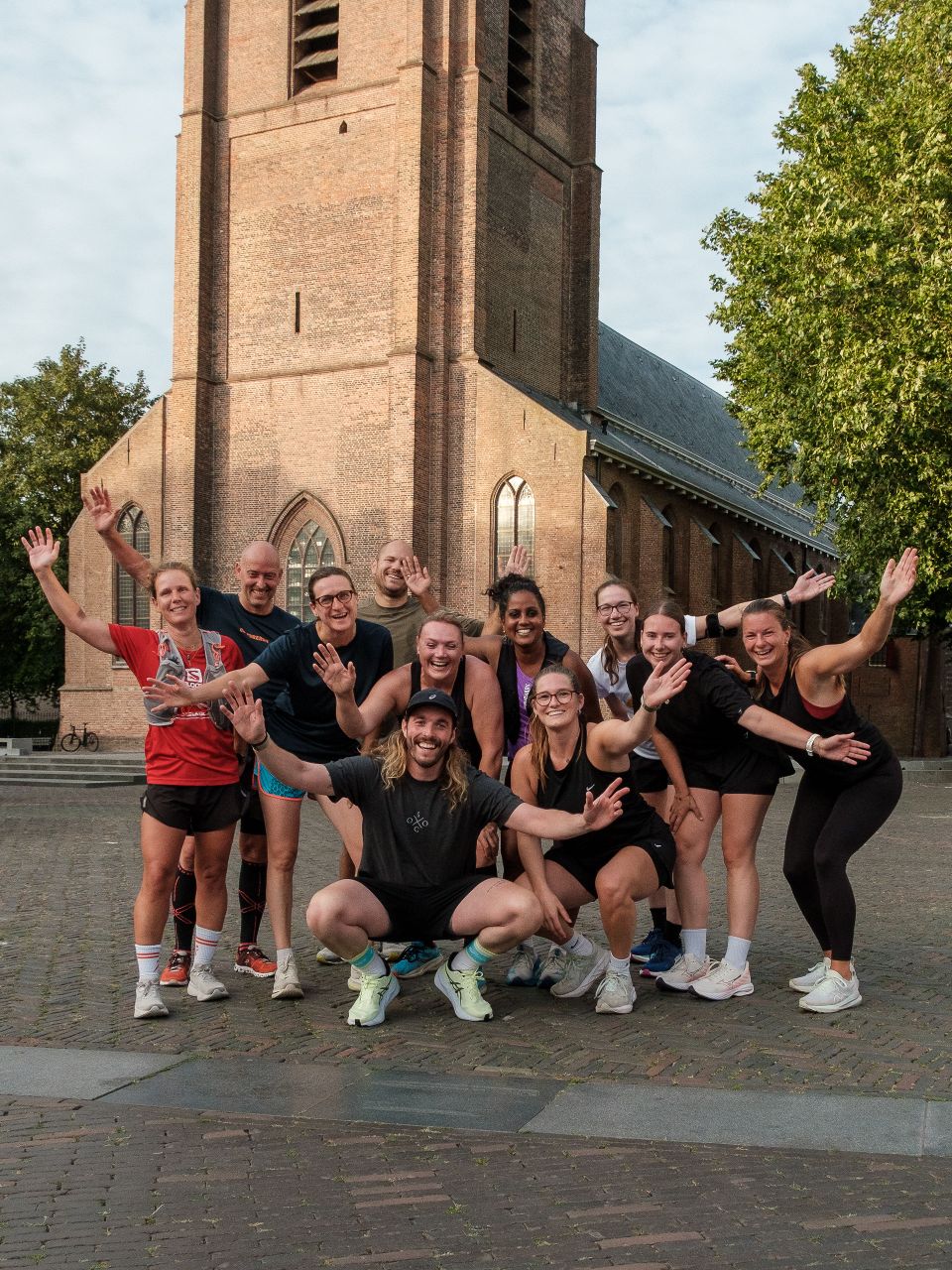 Kerkplein met stadskerk in Woerden, Groene Hart, groepsfoto van deelnemers aan een social run van de Offline Outside Social Club die na het hardlopen poseren op het plein voor de monumentale bakstenen kerk.