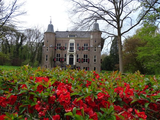 Voorjaarsaanzicht van Landgoed Linschoten met het statige historische landhuis omringd door groen en felrode bloesems op de voorgrond; sfeervolle natuur, buitenplaats en erfgoed in het Groene Hart.