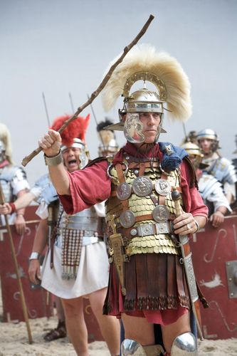 Romeinse bevelhebber in goudkleurig harnas en witte helm met pluim geeft instructies tijdens een re-enactment in Archeon, met soldaten in formatie op de achtergrond.