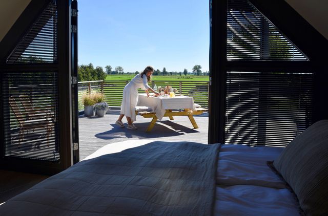 Bed & breakfast Bedje in de Polder in Montfoort, Groene Hart. Uitzicht vanuit een stijlvolle slaapkamer op een zonnig terras waar een ontbijt wordt klaargezet, met weidse groene weilanden en het polderlandschap op de achtergrond.