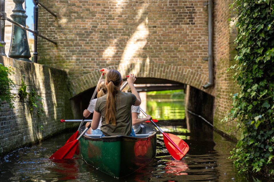 Buitenactiviteit kanoën in Gouda, Zuid-Holland, Groene Hart. Kinderen varen met een kano door een smalle gracht onder een historische brug, een populaire vorm van waterrecreatie en actief gezinsuitje in de historische binnenstad.