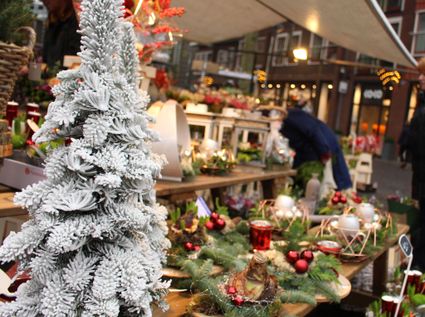 Kerstmarkt in Woerden, Groene Hart, provincie Utrecht, met een besneeuwde kerstboom, feestelijke kerststukken, rode kerstballen en sfeervolle verlichting bij een bloemenkraam in het centrum.
