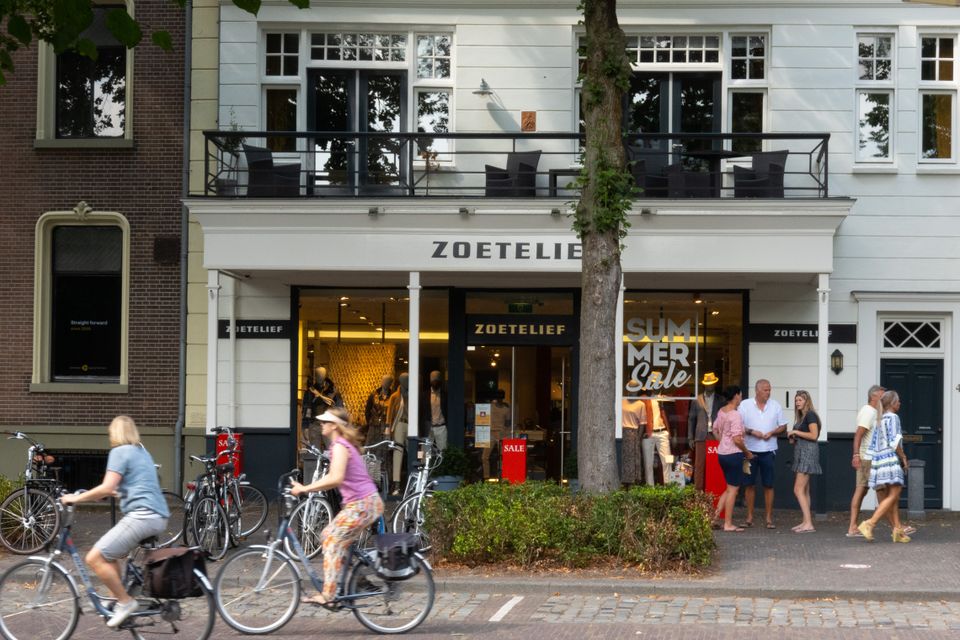 Witte gevel met balkon en etalage en winkelend publiek.