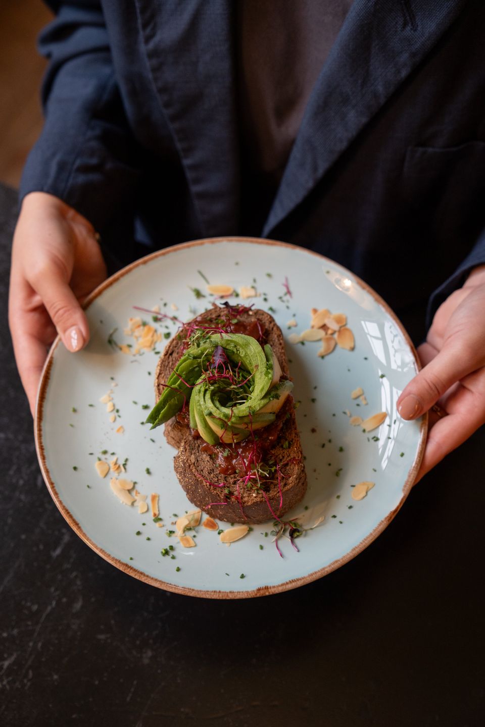Een persoon toont een bord met een smakelijk avocado-broodje.