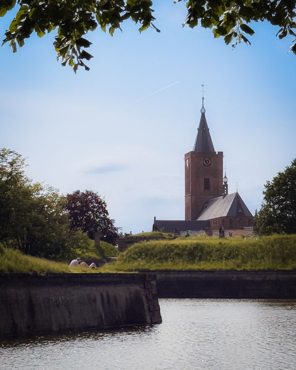 Vestingstad Naarden met op de voorgrond bomen, water en de vestingwallen, op de achtergrond de kerk van Naarden