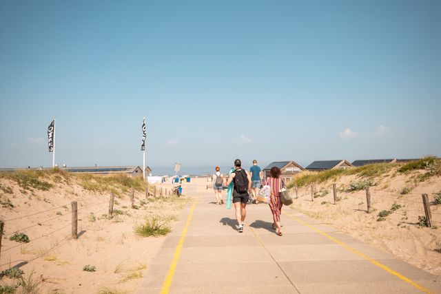 Sfeerbeeld van strandgangers die richting het strand van Katwijk wandelen met op de achtergrond een strandpaviljoen.