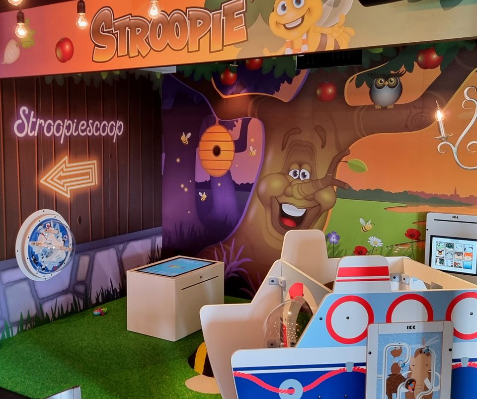 Restaurant De Strooppot in De Hoef, Groene Hart. Kleurrijke kinderspeelhoek met interactieve spellen, vrolijke wandillustraties van dieren en de Stroopiescoop.
