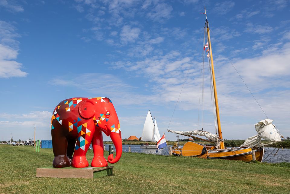 Een beeld van een olifant in het Friese landschap met ernaast in het water een skûtsje.